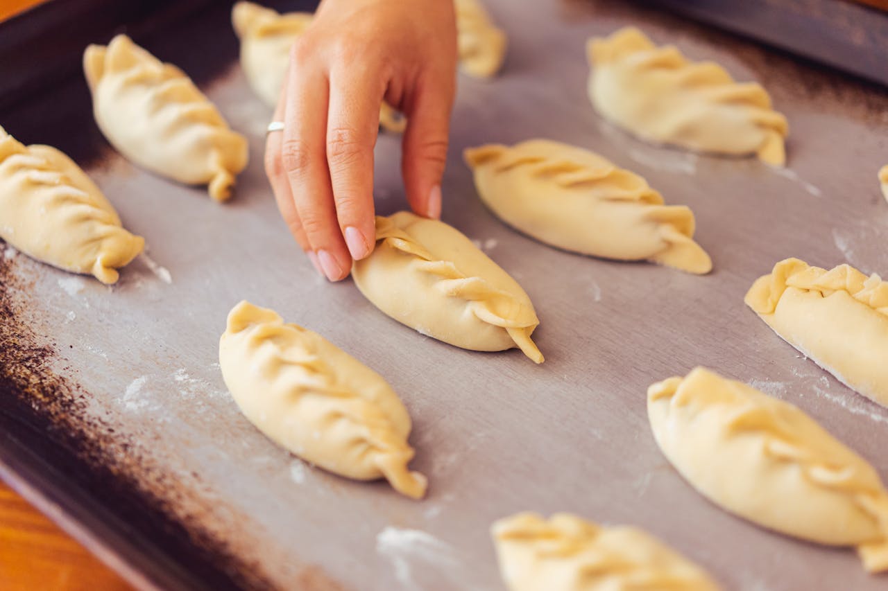 Hand placing raw empanadas on a tray, capturing the essence of Argentine food preparation.