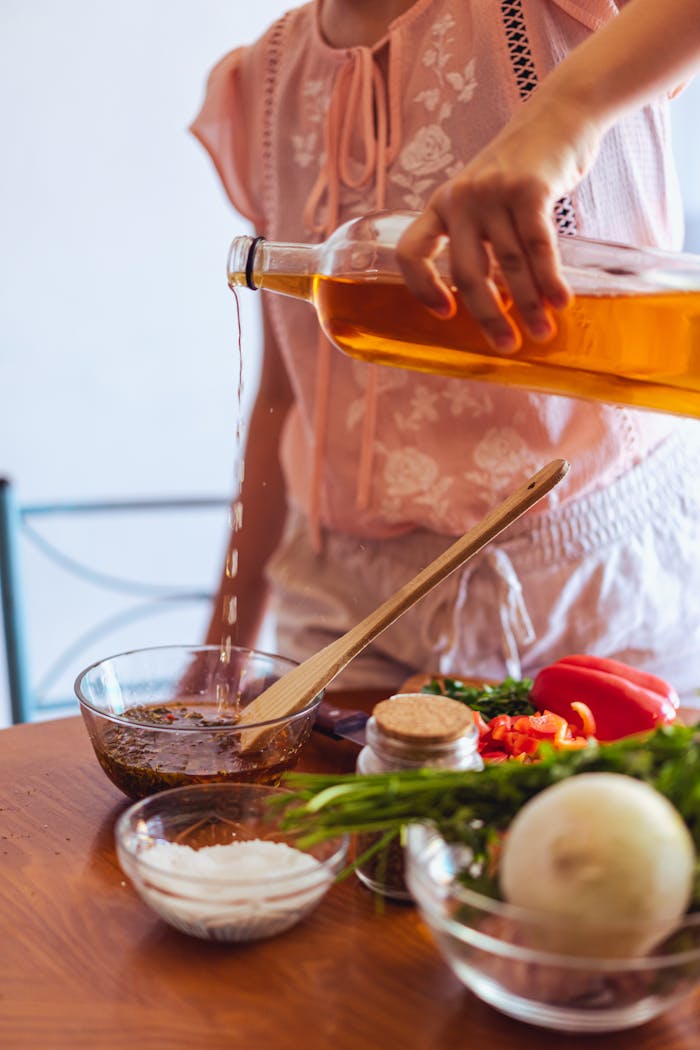 Person pouring vinegar for traditional chimichurri preparation with fresh vegetables and spices.